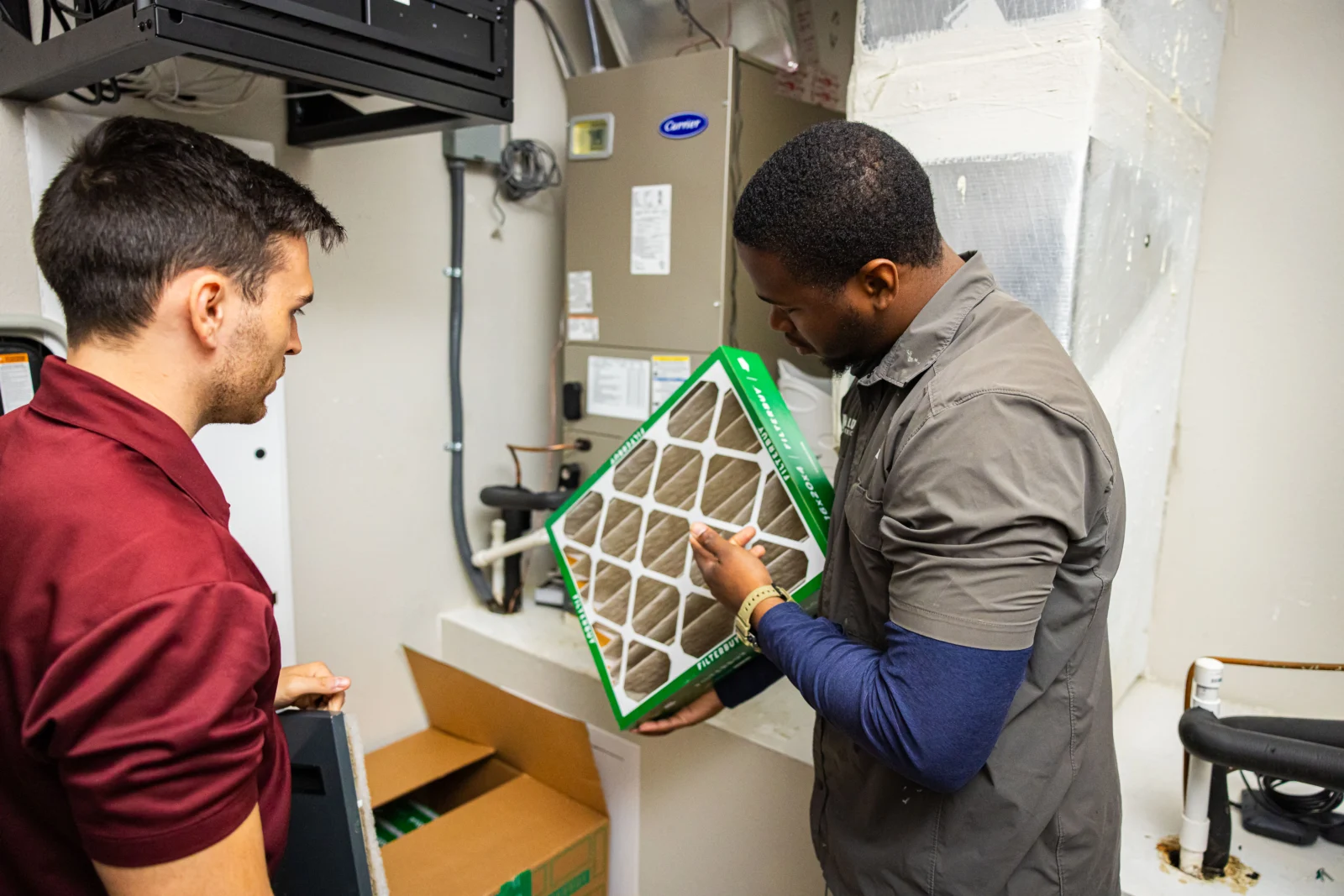 Kalos technician explaining an air filter beside an indoor HVAC system