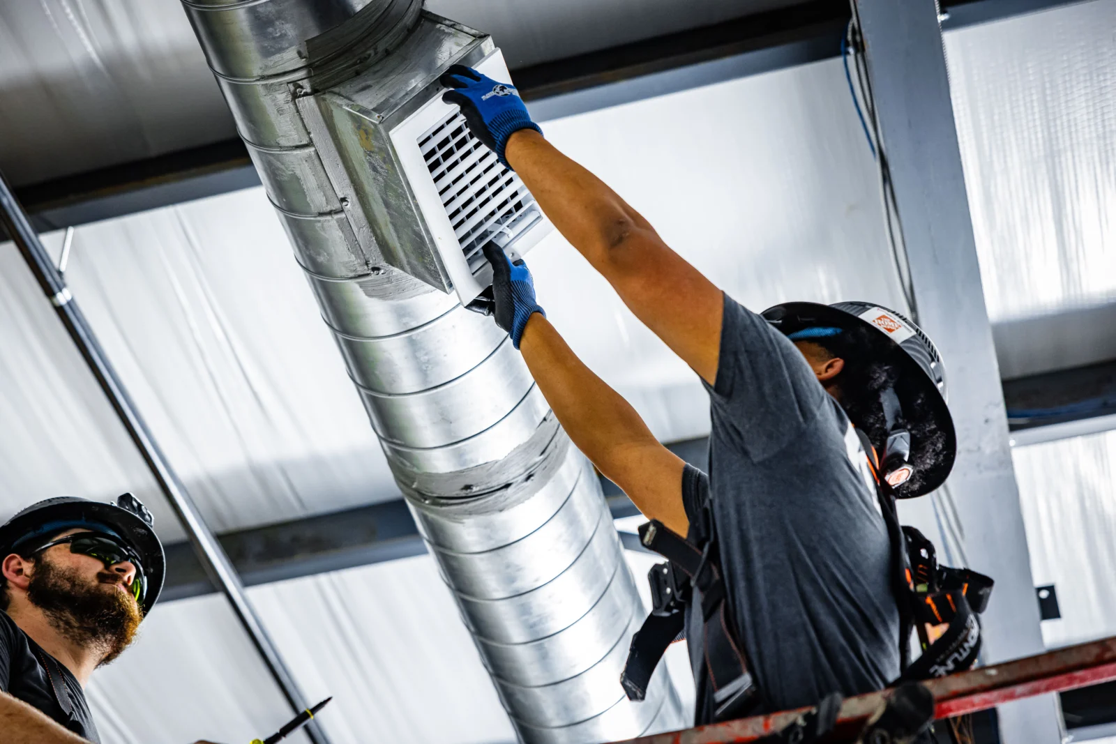 Kalos technicians fitting a ventilation grille in exposed commercial ductwork