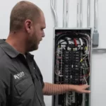 KALOS employee beside an open electrical panel with rows of circuit breakers visible.